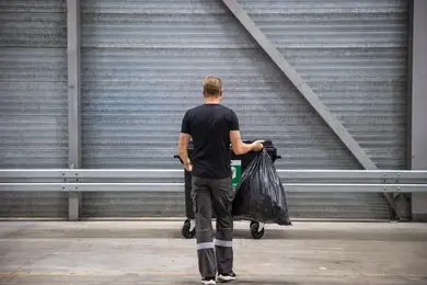 Een medewerker die een zak met restafval weggooit in de rolcontainer.