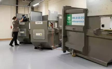 schoonmaker van een hotel gooit vuilniszak in miniperscontainer.