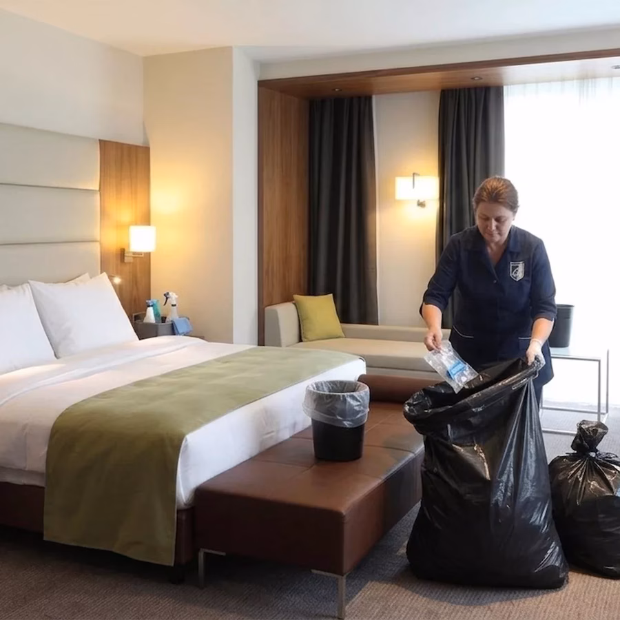 Schoonmaker leegt prullenbakken in vuilniszak in hotelkamer.