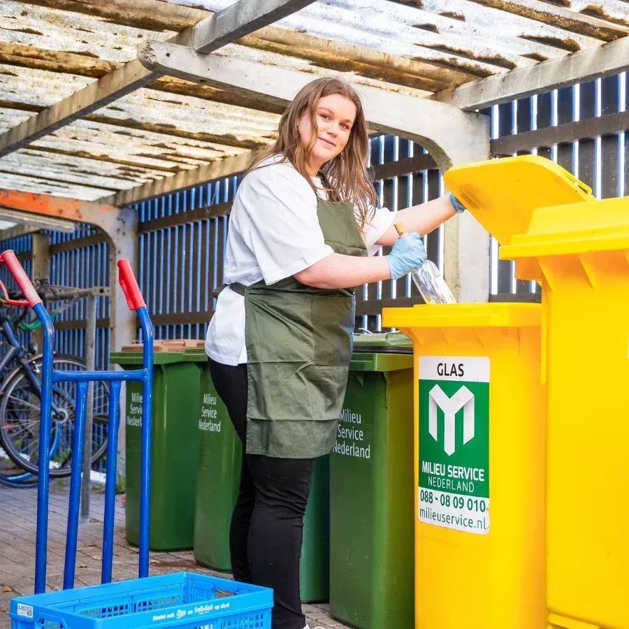 Glas wordt in een glascontainer gegooid door een horecamedewerker