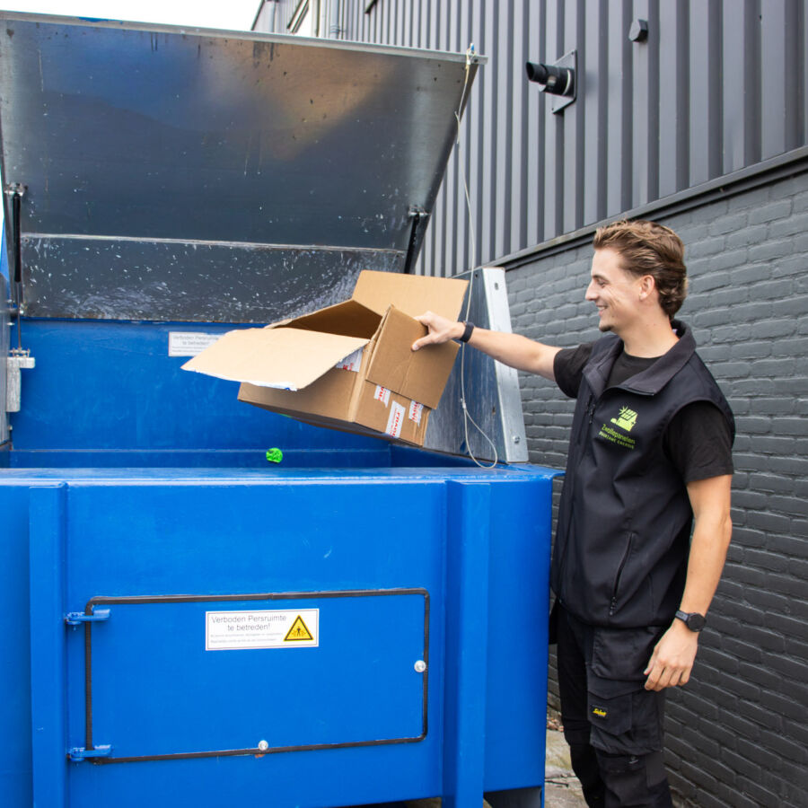 De eigenaar van Zwollepanelen gooit karton in een karton perscontainer die naast zijn bedrijfspand staat.